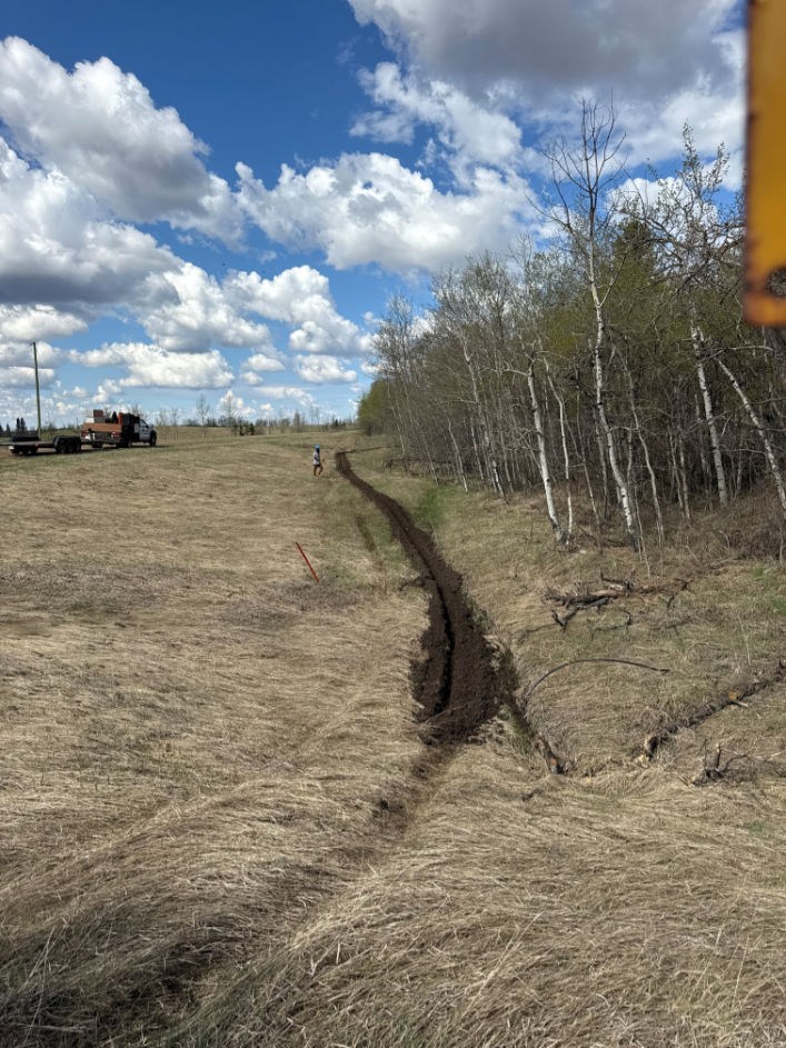 Bergen Brothers Daylighting chain trenching for underground utility installation along a rural tree line.