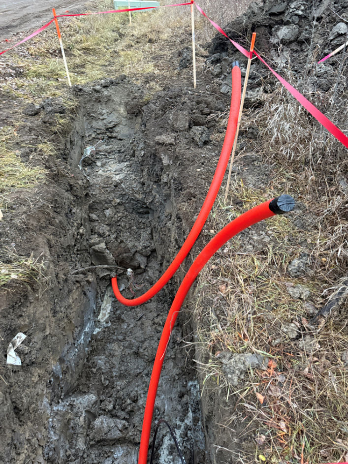 Exposed utility trench with red conduit installed during underground utility work.